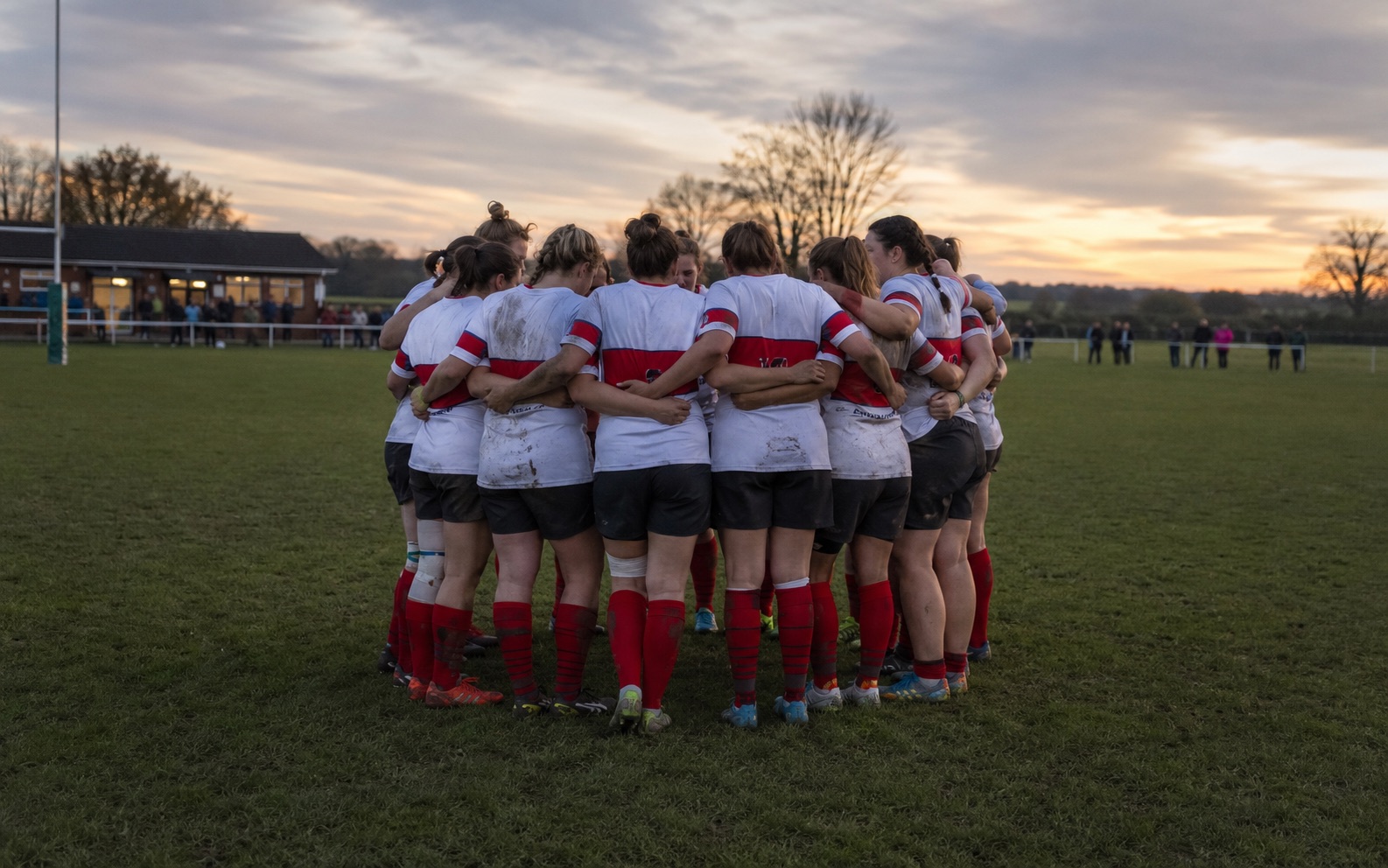 Community rugby team in a huddle on the pitch at sunset